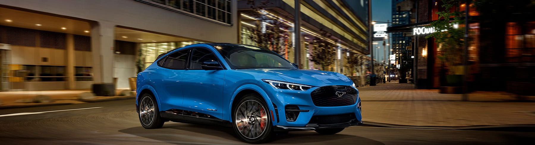 Ein blauer Elektro-Geländewagen fährt nachts auf einer Stadtstraße, mit beleuchteten Geschäften im Hintergrund.