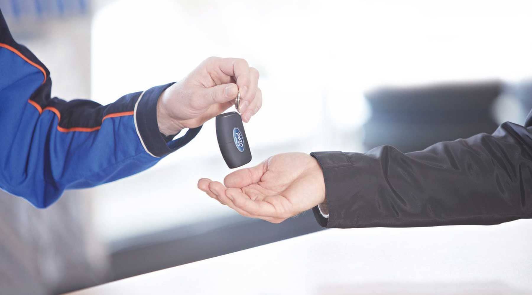 Eine Hand übergibt einen Autoschlüssel mit Ford-Logo an eine andere geöffnete Hand.
