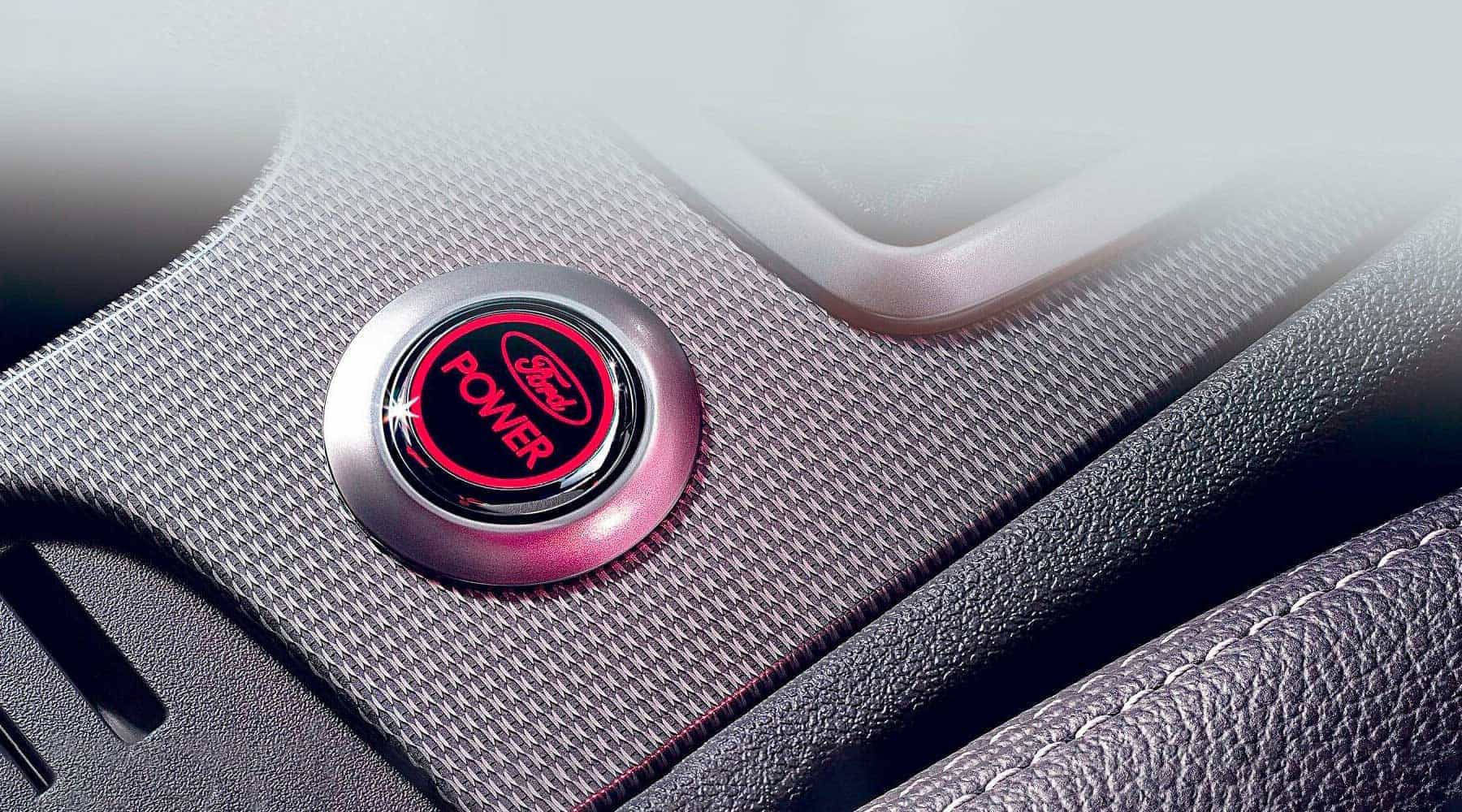 Nahaufnahme eines runden Knopfs mit rotem Ford-Logo und Schriftzug 'POWER' auf einer strukturierten Oberfläche.