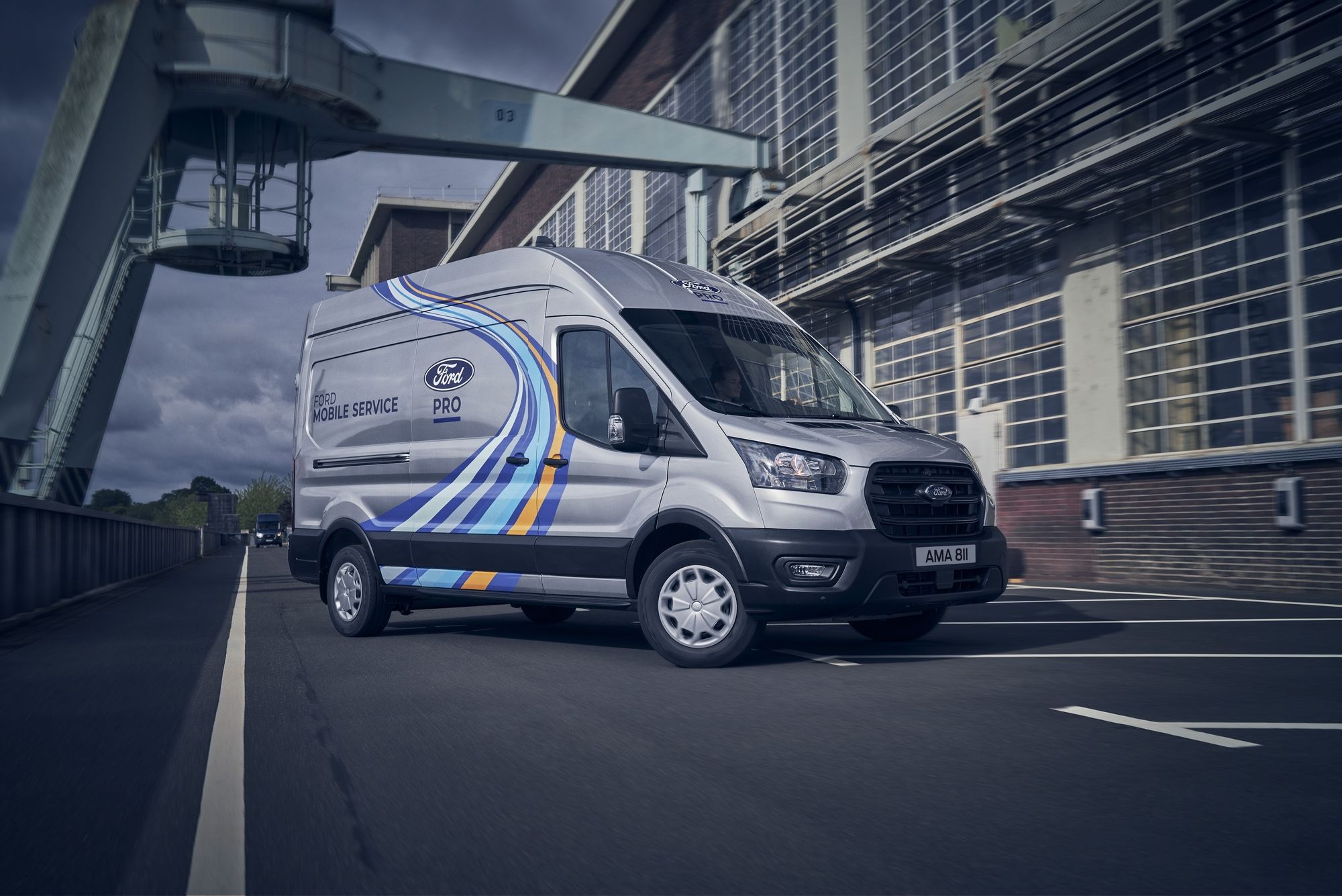 Weißer Ford-Transporter mit blauen und gelben Streifen und Aufschrift "Mobile Service Ford Pro" fährt auf einer Straße